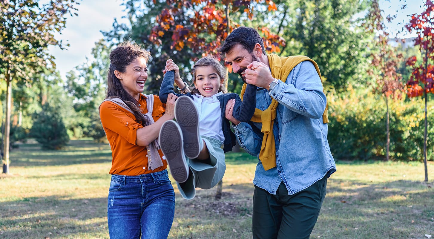 A family laughing and having fun in a vibrant park, surrounded by greenery and engaging in playful activities.